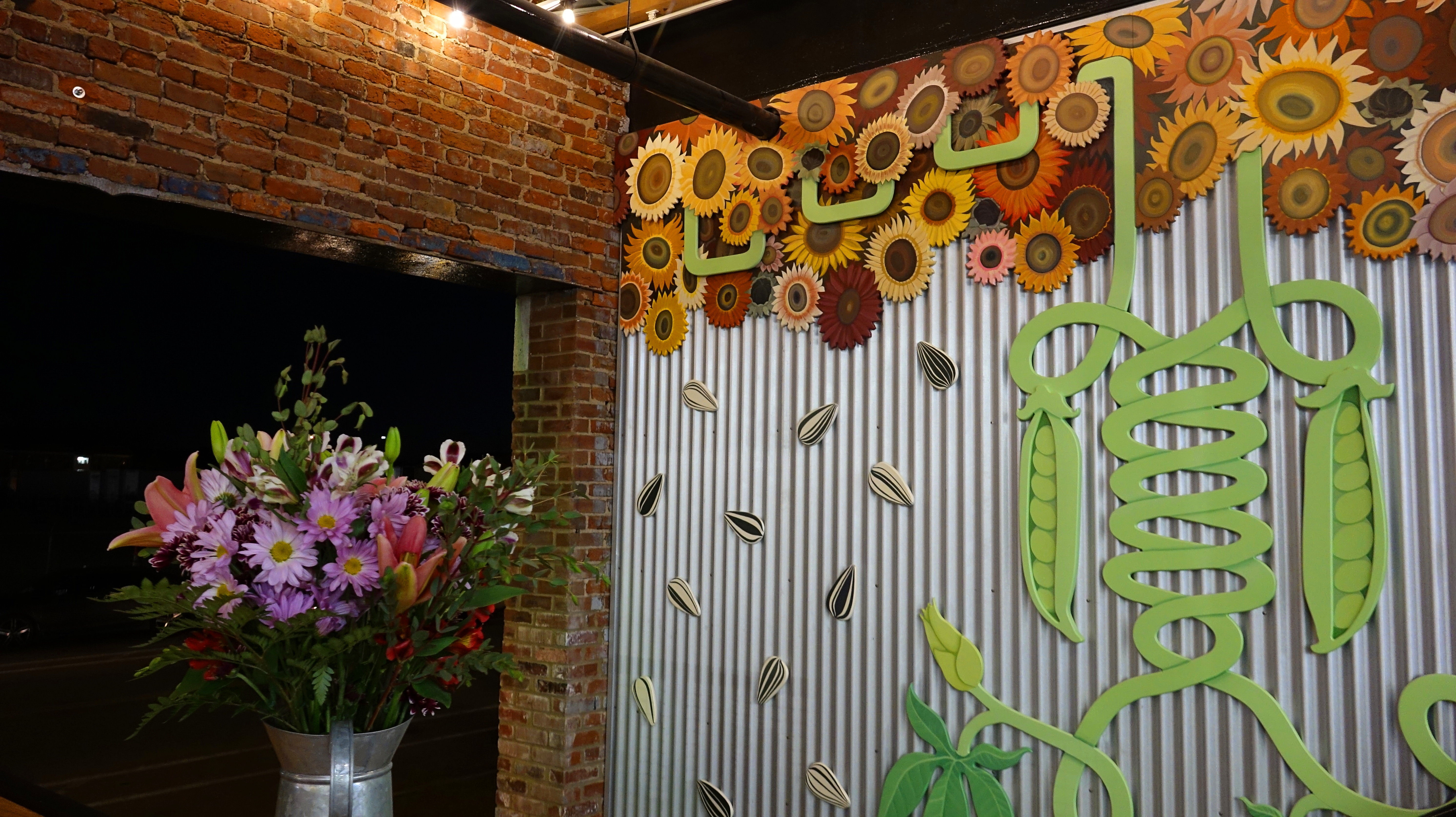 Emily C. Thomas, Virtual Studio Visit, August 2022: A pipe from the building runs through the sunflower panel, linking the wall mural to the surrounding architecture.