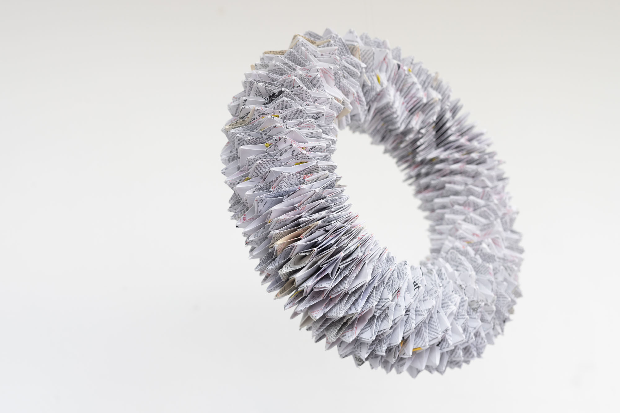 Jocelyn Mathewes, Symptoms/Side-Effects, 2020-2024, spiraling paper loop of individual origami elements made from prescription sheets, suspended 2020-2024, 14” x 14” Jocelyn Mathewes, Symptoms/Side-Effects, 2020-2024, spiraling paper loop of individual origami elements made from prescription sheets, suspended 2020-2024, 14” x 14”